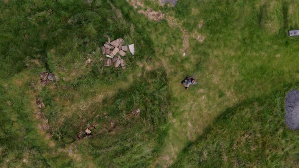 Aerial of a Man Walks Through the Green Meadow Towards Little Black House