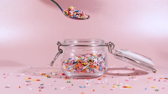 Colorful Candy Confectionery Run Poured Into a Jar Glass on Pink Background