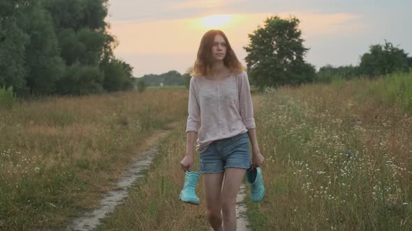 Girl Walking on Rural Road with Boots in Her Hands