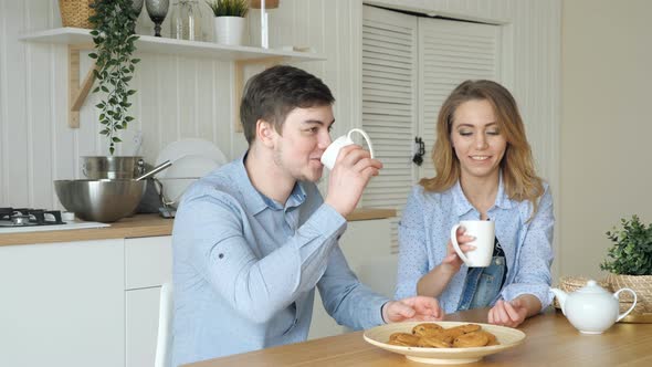 Blond Girl and Guy Have Breakfast Drinking Tea in Kitchen