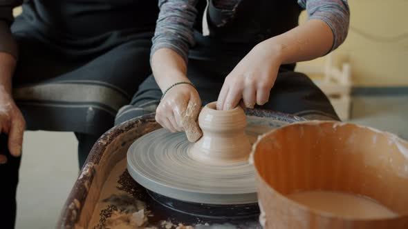 Close-up of Child's Hands Making Pot From Clay on Throwing Wheel Under Guidance of Adult Potter