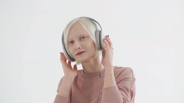 Young Albino Girl in the White Earphones Listening To Music. Girl Albino Casting in a Music Studio