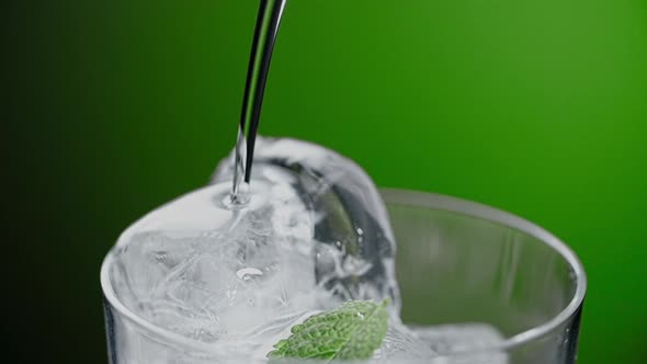 Alcohol is Being Poured in Slow Motion to the Ice Cubes in Cocktail Glass with Drink Ingredients