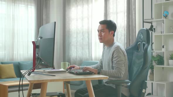 Asian Man Using Desktop Computer On A Table For Working At Home