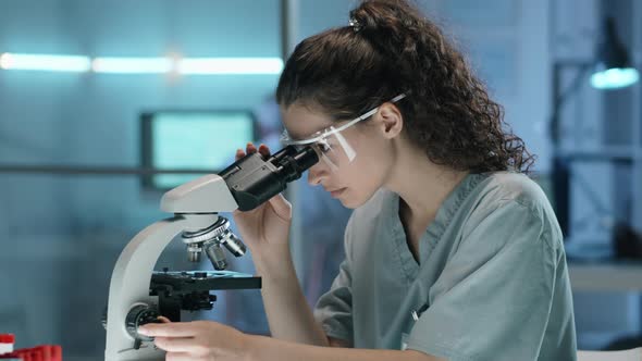 Young Female Scientist Using Microscope and Taking Notes