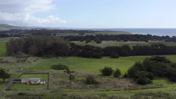 Aerial: Half Moon Bay beach and a farm surrounded by trees, flying forward.