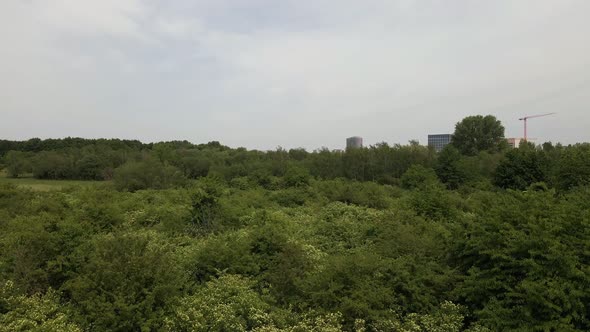 Industrial buildings behind a lush deciduous forest in Eschborn, Germany. Aerial pedestal shot