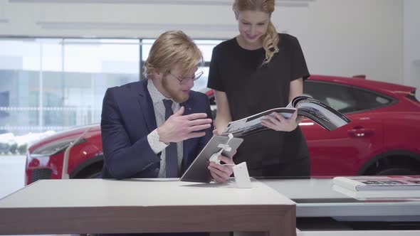 Successful Business Woman Scrolls Through the Catalog with Vehicles Standing Near a Stylish Salesman