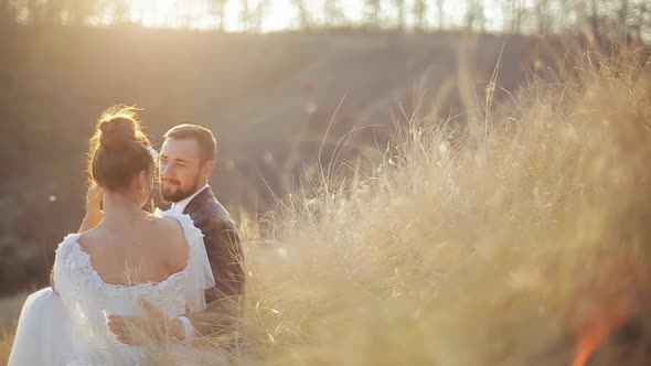 Cute Wedding Couple Is Sitting on the Yellow Grass of a Deserted Field, Communicating and Enjoying