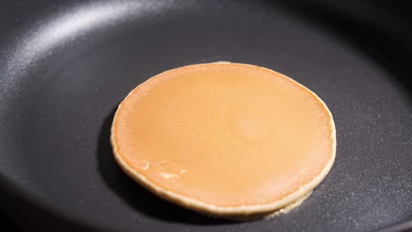 Frying pancake in black frying pan.