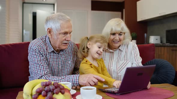 Grandfather and Grandmother Sitting in Living Room and Teaching Small Granddaughter Using Laptop