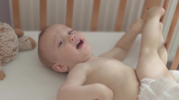 Portrait of Crying Screaming Naked Baby Infant Lying Sitting in Crib Cot Cradle