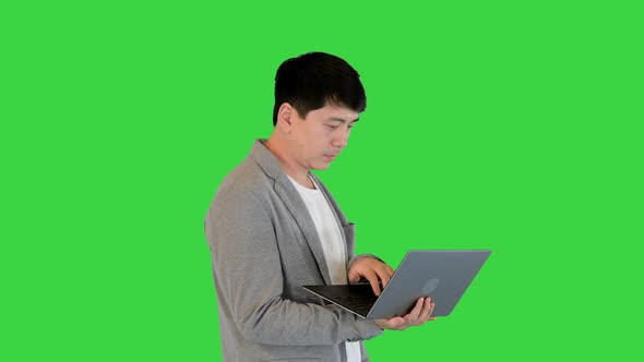 Young Asian Man Types Something Fast on His Laptop and Breathes Out on a Green Screen Chroma Key