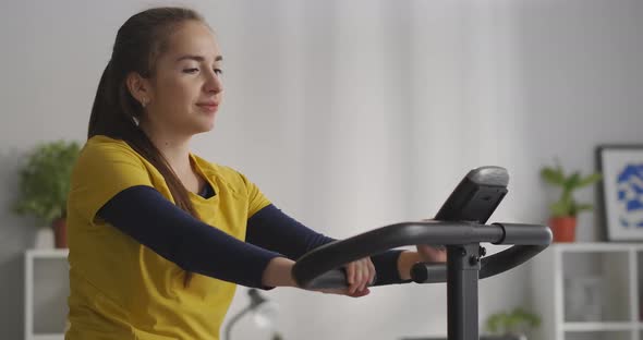 Calm Young Woman Is Exercising with Stationary Bicycle at Home Sport Activity and Healthy Lifestyle