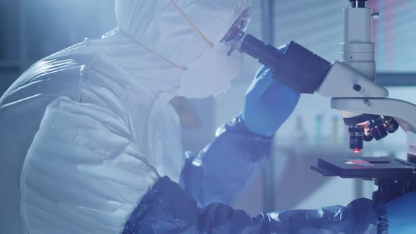 Male Scientist in Protective Suit Using Microscope and Posing for Camera