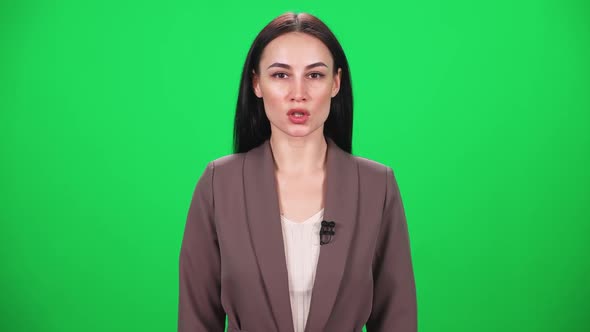 Woman Reporter in Suit Looks Into the Camera and Speaks Into a Microphone on a Green Background