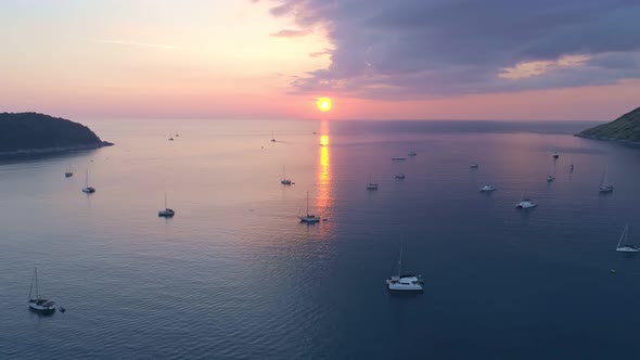 Colorful sunset above the sea surface with sail boats. Aerial view drone fly over Phuket sea