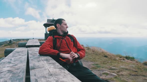 Tourist with Backpack on Top of Mountain Sat Down To Rest at an Old Wooden Table