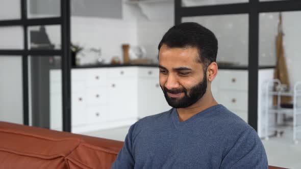 Optimistic Ethnic Man in Casual Wear Using Laptop Sitting on the Couch