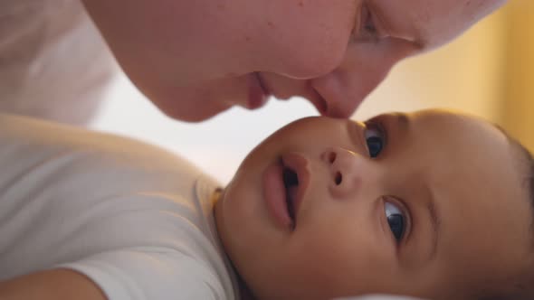 Close Up of Young Happy Mother Playing with Newborn Baby Lying on Bed