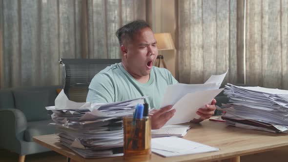 Fat Asian Man Yawning While Working Hard With Documents At The Office