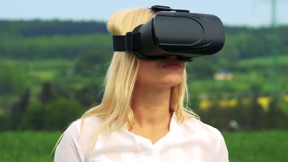 Young Attractive Blond Woman Uses Virtual Reality Glasses - Countryside in the Background - Closeup