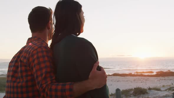 Happy caucasian couple sitting on beach by the sea talking hugging