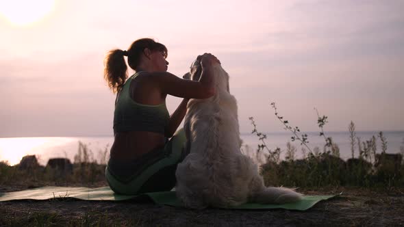 Sporty Female Caressing Dog on Sea Coast at Sunset