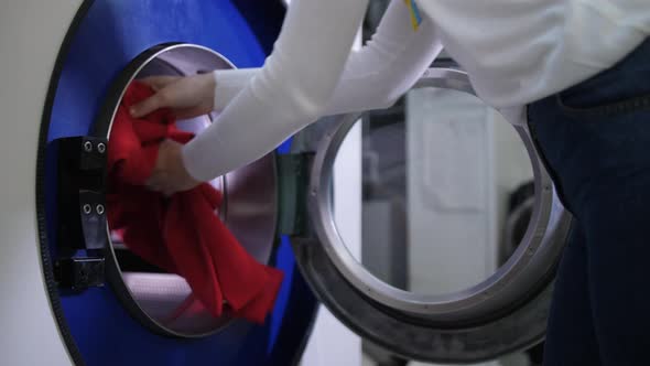 Worker's Hands Loading Jacket Into Washing Machine
