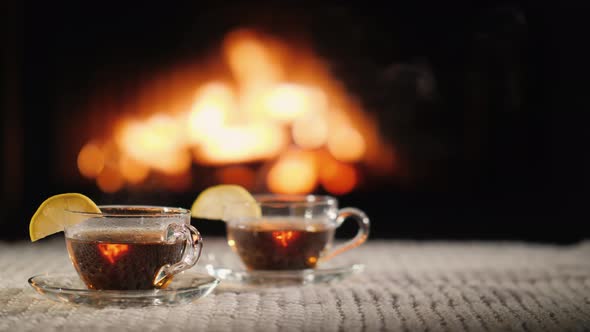 Two Cups of Hot Tea with Lemon on a Table Against the Background of the Fireplace