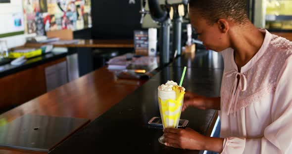 Happy woman talking on mobile phone while having milkshake