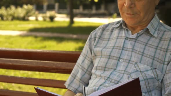 Senior Man Writes in His Notebook on the Bench