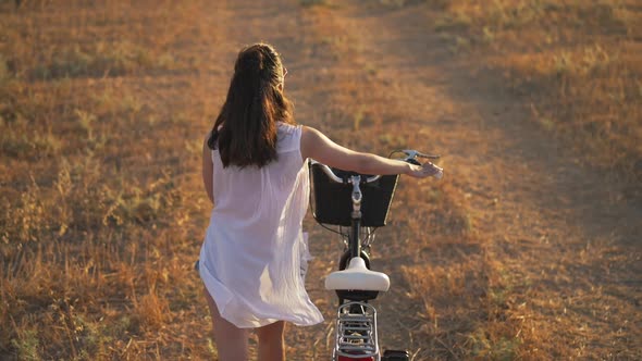 High Angle View Young Slim Woman with Bike Walking in Slow Motion at Sunset on Rural Field