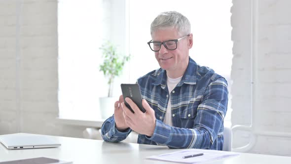 Cheerful Casual Middle Aged Man Using Smartphone in Office 