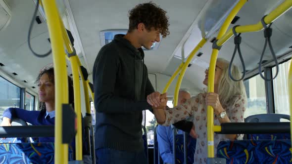 Male commuter helping mature commuter to get up while travelling in bus 4k