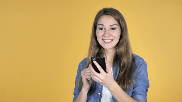 Pretty Woman Excited for Success While Using Smartphone Isolated on Yellow Background