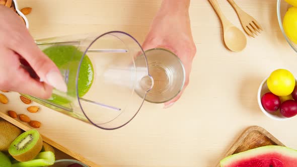 Pouring Green Detox Smoothie Into Glass From Blender on Table in the Kitchen Top View