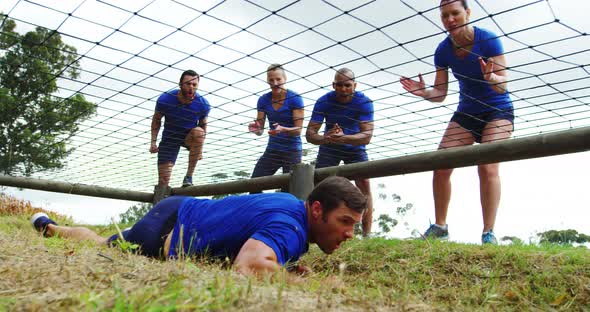 Fit man crawling under the net during obstacle course while fit people cheering