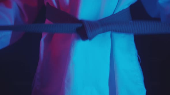 A Little Boy Doing Taekwondo in Neon Lighting  Tying Up the Belt and Showing Moves with His Hands