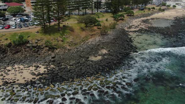 Descending  quickly to sea level over rocky beach, bright sunshine, crashing waves