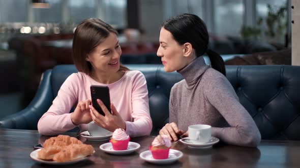 Two Female Friends Chatting Looking Photo Use Smartphone at Cafeteria