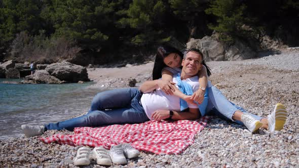 Husband and wife spend the weekend, hugging and having picnic near sea on sunny summer day.