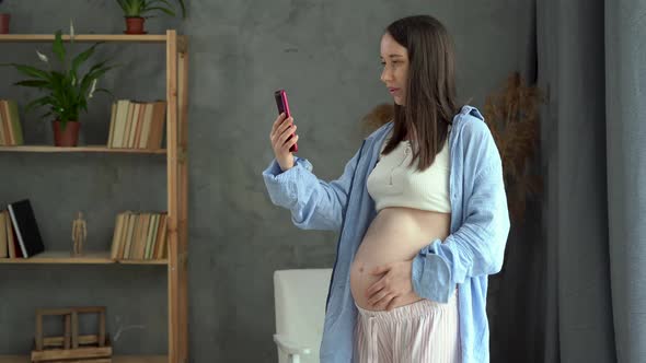 Pregnant Caucasian Woman Standing in the Room Having a Video Conference with a Doctor on a Mobile