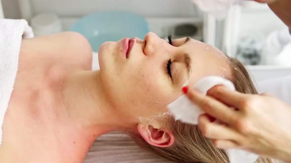 Beautician cosmetologist cleans removes face peeling beauty mask with napkins.