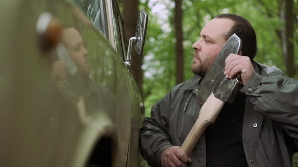 Slow Motion Of Casual Strong Man Has Shave with Ax Near Classic Car in Wild Deciduous Forest.