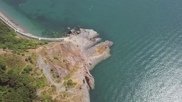 Overhead view of the beach in Torquay with its blue water and tall cliffs. Rock and woodland is visi