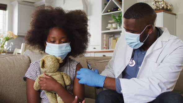 African american doctor wearing face mask injection covid-19 vaccine to girl at home