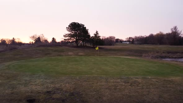 Tracking shot moving forward over golf course during sunrise. Close up fly by of yellow flag at the