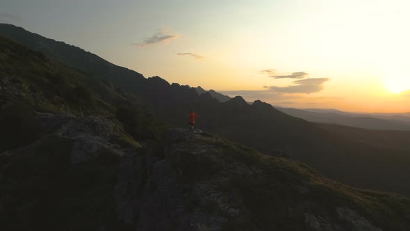 Hiker Enjoying Nature and Freedom at Mountain Top Standing at Rocky Precipice Looking the Sunset