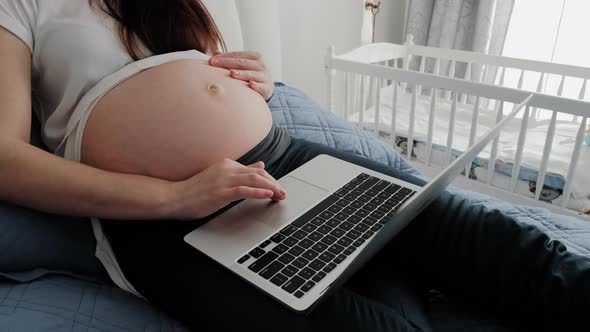 Close Up Shot of Pregnant Woman Resting on a Sofa at Home and Working Remotely with Laptop Computer